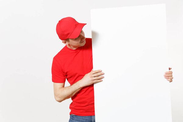 Delivery young man in red uniform isolated on white background. Male courier in cap, t-shirt holding big white empty paper billboard. Copy space advertisement. Place for text image. Advertising area