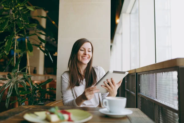 Yalnız büyük kahve dükkanında tablo penceresinde yakınındaki kapuçino, bardak ile oturan kadın kek, restoranda serbest zaman sırasında rahatlatıcı. Pc tablet bilgisayar dinlenme kafede çalışan erkek. Yaşam tarzı kavramı