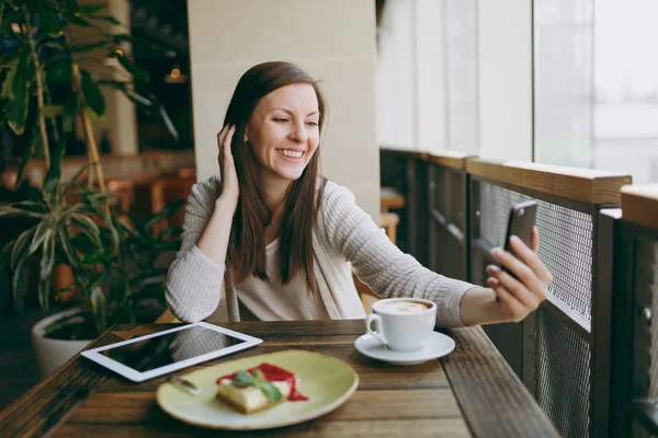 Fincan kapuçino, kafede oturan kadın cep telefonunda selfie yapıyor, restoranda serbest zaman sırasında rahatlatıcı kek. Tablet bilgisayar dinlenme kafede çalışan erkek. Yaşam tarzı kavramı