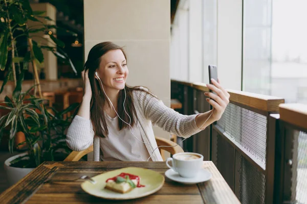 Yalnız fincan kapuçino, kafede masada oturan genç kadın kek, restoranda serbest zaman sırasında rahatlatıcı. Genç selfie cep telefonu, yapıyor kadın cafede bekletin. Yaşam tarzı kavramı