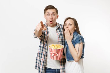 Genç çift, kadın ve tarihte film film izlerken, kova patlamış mısır holding, işaret parmağı kamera işaret ve beyaz arka plan üzerinde izole ağız kapsayan adam şok. Sinema kavramı duygular