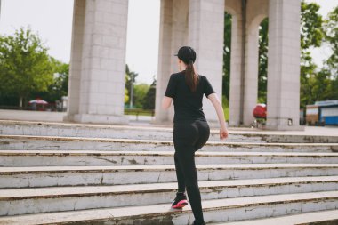 Arkadan görünüşü genç atletik güçlü esmer kız siyah üniforma giyen ve cap city Park açık havada merdivenlerde tırmanma çalıştırmadan önce ısınma spor egzersizleri, yapıyor. Fitness, sağlıklı yaşam konsepti