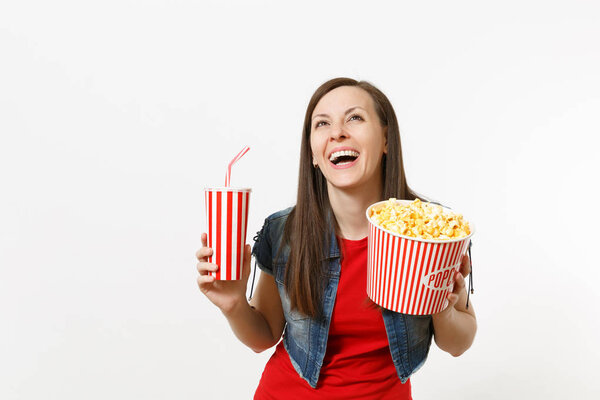 Portrait of young funny laughing attractive woman watching movie film, holding bucket of popcorn and plastic cup of soda or cola, looking up isolated on white background. Emotions in cinema concept