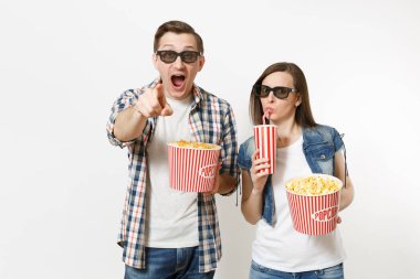Young couple, woman and man in 3d glasses watching movie film on date, holding bucket of popcorn, cup of soda or cola, pointing index finger on camera isolated on white background. Emotions in cinema clipart