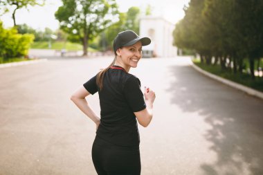 Genç gülümseyen güzel esmer kız siyah üniforma giyen ve eğitim, spor egzersizleri yapıyor ve çalıştırma, city park açık havada yolda seyir sırt kap atletik. Fitness, sağlıklı yaşam konsepti