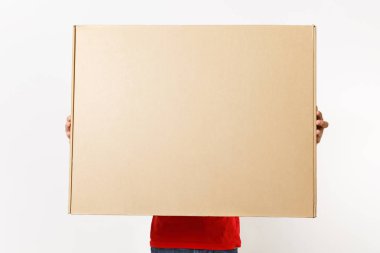 Beyaz arka plan üzerinde izole kırmızı üniformalı teslimatçı. Erkek şapka, tişört, kot pantolon kurye veya satıcı holding büyük büyük ağır karton kutu çalışıyor. Paket alma. Kopyalama alanı reklam