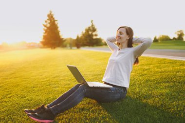 Genç öğrenci rahat kıyafetler esmer kadın. Kadın oturuyordu, rahatlatıcı, ellerinizi başınızın koyun. dizüstü pc bilgisayar yeşil çimenlerin üzerinde açık havada Güneş çim zemin. Mobil ofis. Serbest iş kavramı