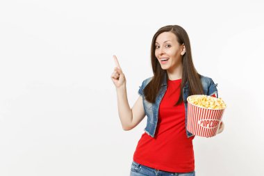 Film film izlerken, kova patlamış mısır holding, beyaz arka plan üzerinde izole boşaltmak işaret parmağı yukarıyı rahat kıyafetler içinde genç gülümseyen güzel kadın portresi. Sinema kavramı duygular