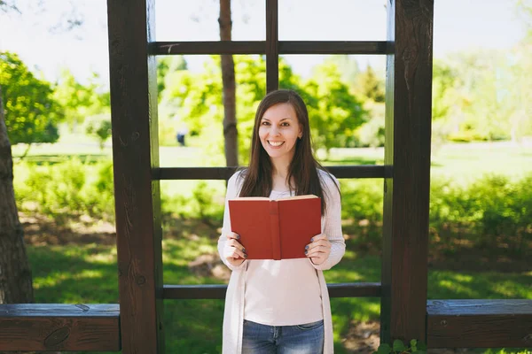 Portrait of beautiful calm peaceful young woman wearing light casual clothes relaxing, reading book. Smiling female resting in city park in street outdoors on spring nature. Lifestyle, concept
