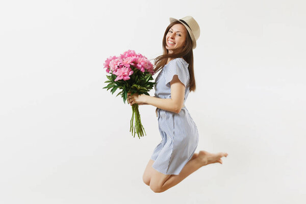 Full length of happy fun young woman in blue dress, hat holding bouquet of pink peonies flowers, jumping isolated on white background. St. Valentine's Day, International Women's Day holiday concept