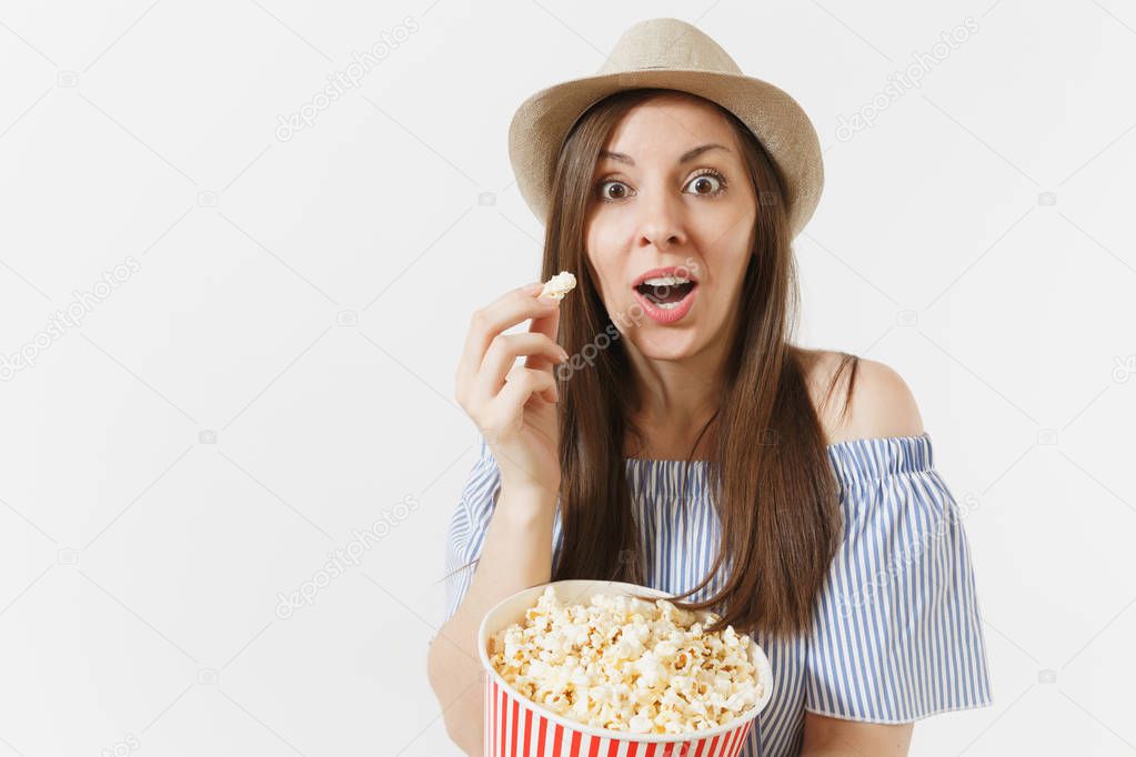 Surprised fun woman in blue dress, hat watching movie film eating popcorn from bucket isolated on white background. People, sincere emotions in cinema, lifestyle concept. Advertising area. Copy space