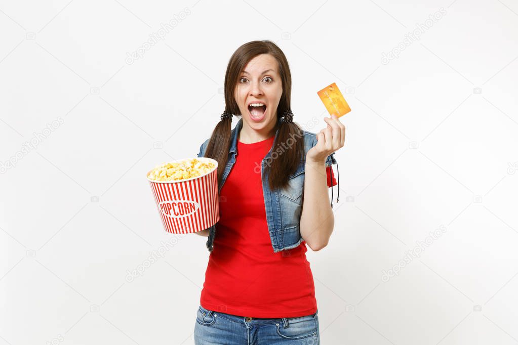 Portrait of young overjoyed attractive brunette woman in casual clothes watching movie film, holding bucket of popcorn and credit card isolated on white background. Emotions in cinema concept