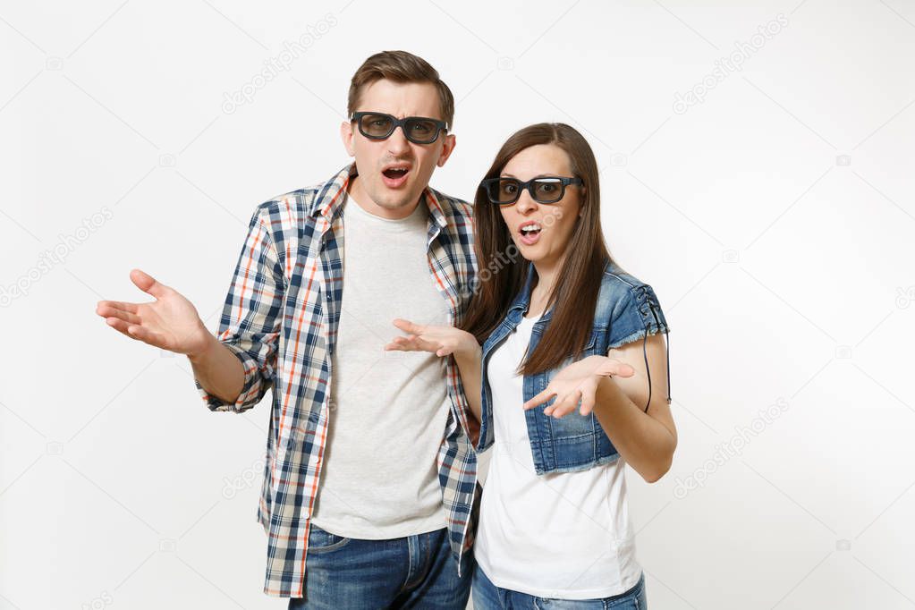 Young irritated dissatisfied couple, woman and man in 3d glasses and casual clothes watching movie film on date and spreading hands isolated on white background. Emotions in cinema concept