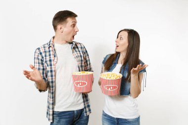 Young shocked couple, woman and man in 3d glasses and casual clothes watching movie film on date, holding buckets of popcorn, spreading hands isolated on white background. Emotions in cinema concept clipart