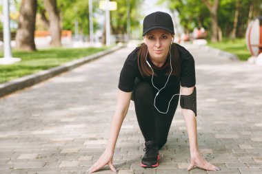Genç atletik güzel esmer kız siyah üniforma ve düşük başlamadan önce şehir park açık havada yolda çalışan, eğitim, müzik dinlerken kulaklık ile kap. Fitness, sağlıklı yaşam konsepti
