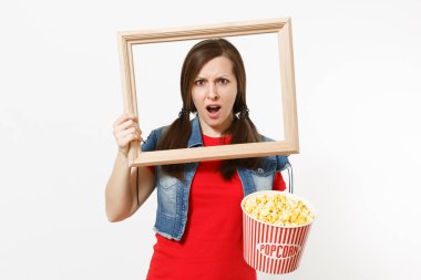 Film film izlerken, patlamış mısır ve resim çerçeve beyaz arka plan üzerinde izole kova tutarak rahat kıyafetler içinde genç şok çekici esmer kadın portresi. Sinema kavramı duygular