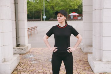 Genç atletik güzel esmer kız siyah üniforma ve spor egzersizleri yapıyor cap city park açık havada duran çalıştırmadan önce ısınma yoğunlaşmıştır. Fitness, sağlıklı yaşam konsepti