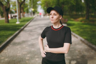 Siyah üniforma ve ayakta, dinlenme ve bir kenara Şehir Park açık havada çalışan, eğitimden sonra seyir kap içindeki genç atletik güzel esmer kız portresi. Fitness, sağlıklı yaşam konsepti