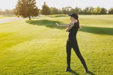 Golf sahası Park yeşil çim üzerinde açık havada güneşli yaz gününde çalıştırmadan önce uzanan genç atletik kız siyah üniforma, Cap ısınma, spor egzersizleri, yapıyor. Fitness, sağlıklı yaşam konsepti