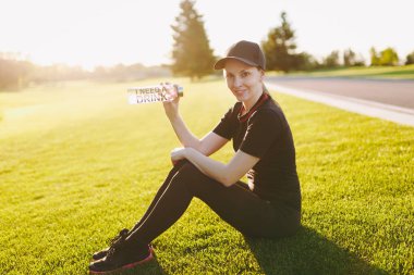 Siyah üniformalı genç kız kap rahatlatıcı yeşil çimenlerin üzerine çalışan, spor egzersizleri sonra içme suyu şişe açık havada güneşli yaz gününde üzerinde dinlenme oturuyor. Fitness, sağlıklı yaşam konsepti