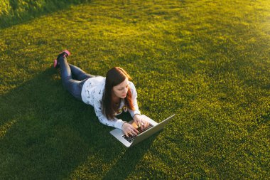 Genç öğrenci rahat kıyafetler içinde kadın akıllı. Çim, dizüstü pc bilgisayar Şehir Park açık havada Güneş çim yeşil çim üzerinde üzerinde çalışıyor yatan kadın. Mobil ofis. Serbest iş kavramı