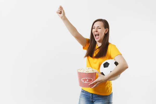 Smiling European young woman, football fan or player in yellow uniform holding soccer ball, bucket of popcorn isolated on white background. Sport, play football, cheer, fans people lifestyle concept