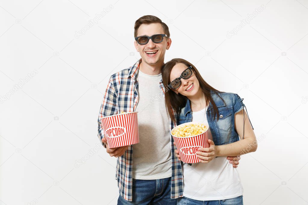 Young happy smiling couple, woman and man in 3d glasses and casual clothes watching movie film on date, holding buckets of popcorn, hugging isolated on white background. Emotions in cinema concept