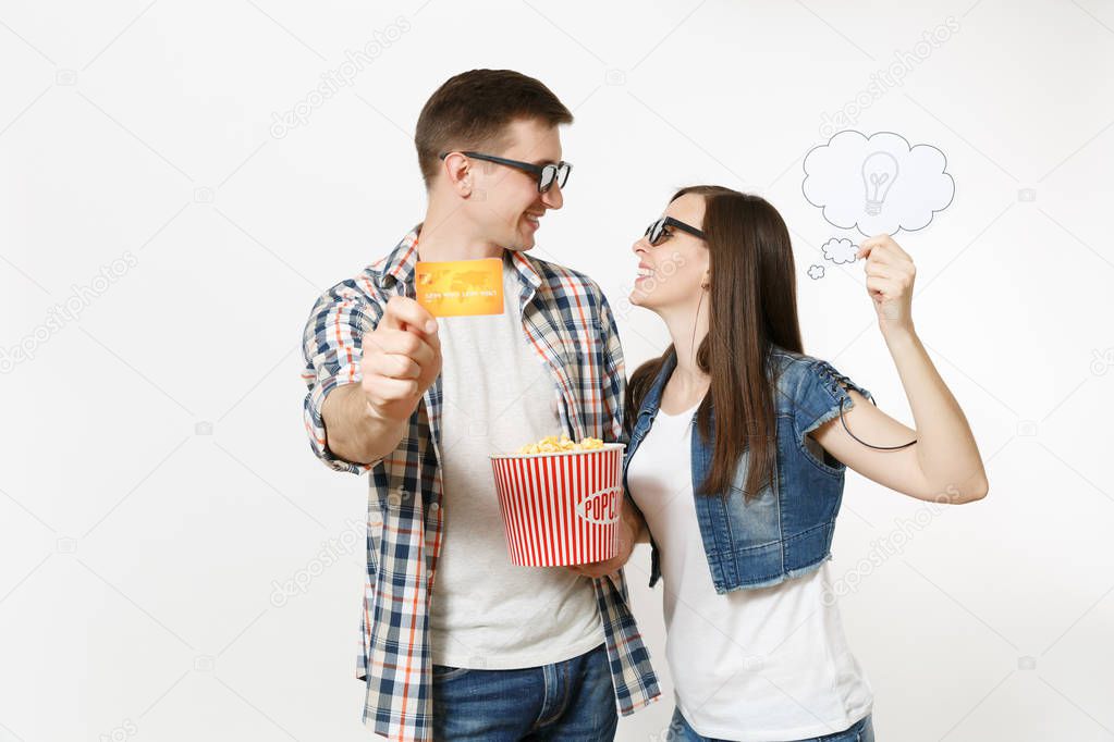 Young couple, woman and man in 3d glasses watching movie film on date holding bucket of popcorn, say cloud with lightbulb, idea and credit card isolated on white background. Emotions in cinema