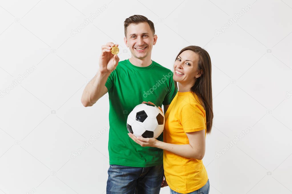 Smiling young couple, woman man, football fans in yellow green t-shirt cheer up support team with soccer ball bitcoin, golden coin isolated on white background. Sport family leisure lifestyle concept