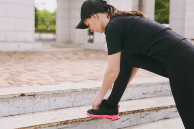 Genç atletik güzel esmer kız siyah üniforma ve cap city Park açık havada merdivenlerde bağlama ayakkabı bağcığı çalıştırmadan önce ısınma spor egzersizleri, yapıyor. Fitness, sağlıklı yaşam konsepti
