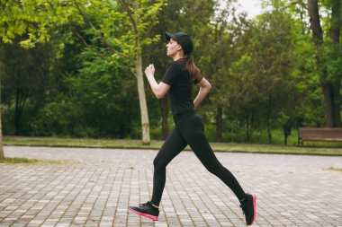 Genç atletik güzel esmer kız siyah üniforma giyen ve kap konsantre eğitim spor yaparken egzersizleri Şehir Park açık havada düz yolda seyir çalıştıran. Fitness, sağlıklı yaşam konsepti