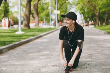 Genç atletik güzel esmer kız siyah üniforma giyen ve müzik dinleme, city Park açık havada yolda çalışan, eğitim önce ayakkabı bağcığı bağlama kulaklık ile kap. Fitness, sağlıklı yaşam tarzı