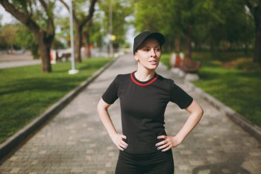 Şehir Park açık havada yolda spor egzersizleri, çalıştırmadan önce ısınma yapıyor genç atletik güzel esmer kız siyah üniforma ve kap ayakta, eğitim. Fitness, sağlıklı yaşam konsepti