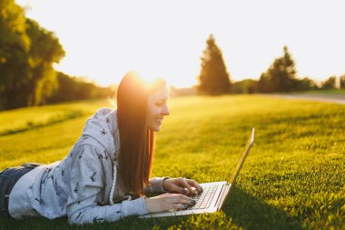 Genç öğrenci rahat kıyafetler içinde kadın akıllı. Çim, dizüstü pc bilgisayar Şehir Park açık havada Güneş çim yeşil çim üzerinde üzerinde çalışıyor yatan kadın. Mobil ofis. Serbest iş kavramı