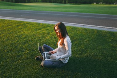 Genç öğrenci kadın rahat kıyafetler. Dizüstü pc bilgisayar Şehir Park açık havada Güneş çim yeşil çim üzerinde çalıştığı yer, çimenlerin üzerinde oturan bir bayan. Mobil ofis. Serbest iş kavramı