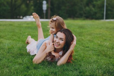 Gülümseyen kadın ışık elbise ve küçük şirin çocuk bebek kız sarılmak, kucaklamak ve çim kalan yalan ve eğlenin. Anne, küçük çocuk kızı. Anneler günü, aşk aile, ebeveynlik, çocukluk kavramı