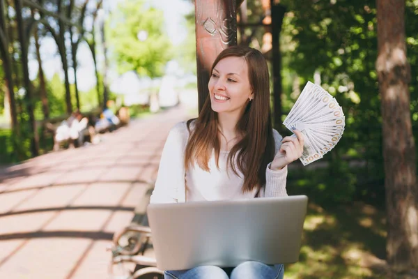 Dolar, nakit para demet tutan genç başarılı işkadını. Şehir Park açık havada doğa üzerinde sokakta modern dizüstü pc bilgisayar üzerinde çalışan kadın. Mobil ofis. Serbest iş kavramı