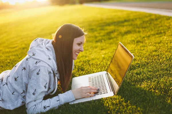Genç öğrenci rahat kıyafetler içinde kadın akıllı. Çim, dizüstü pc bilgisayar Şehir Park açık havada Güneş çim yeşil çim üzerinde üzerinde çalışıyor yatan kadın. Mobil ofis. Serbest iş kavramı