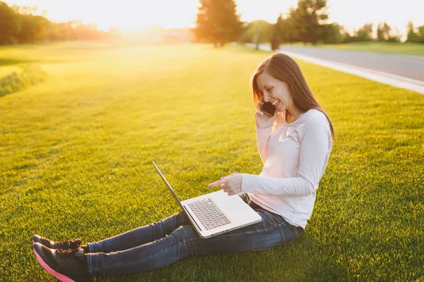 Genç öğrenci rahat kıyafetler içinde kadın akıllı. Dizüstü pc bilgisayar Şehir Park açık havada Güneş çim çimen üzerinde çalıştığı kadın üstünde hareket eden telefon, söz. Mobil ofis. Serbest iş kavramı