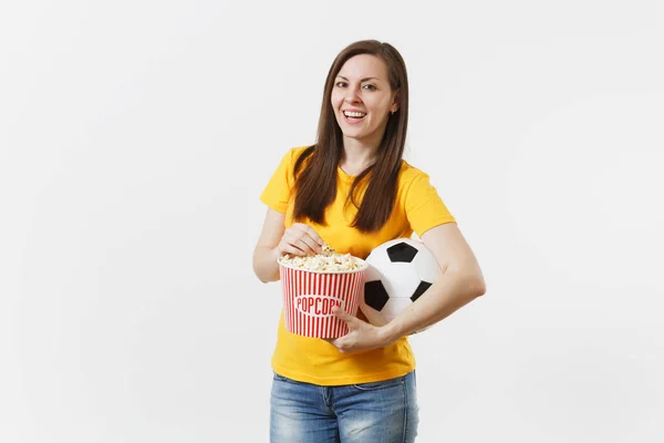 Smiling European young woman, football fan or player in yellow uniform holding soccer ball, bucket of popcorn isolated on white background. Sport, play football, cheer, fans people lifestyle concept