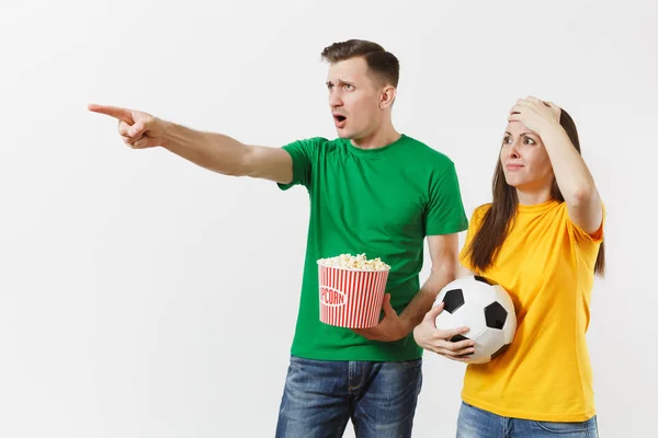 Dissatisfied couple, woman, man, football fans in yellow green t-shirt cheer up support team with soccer ball bucket of popcorn isolated on white background. Sport, family leisure, lifestyle concept