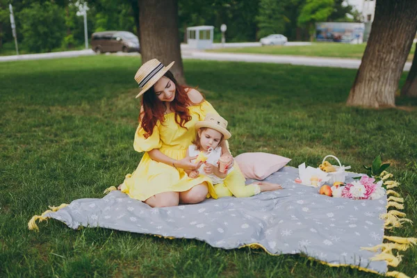 Gülümseyen kadın oyun ve Park, yeşil çimenlerin üzerinde oturup dinlenmek ve tutun sabun köpüğü üfleyici ile küçük şirin çocuk bebek kız sarılmak. Anne, küçük çocuk kızı. Anneler günü, aşk aile, ebeveynlik, çocukluk
