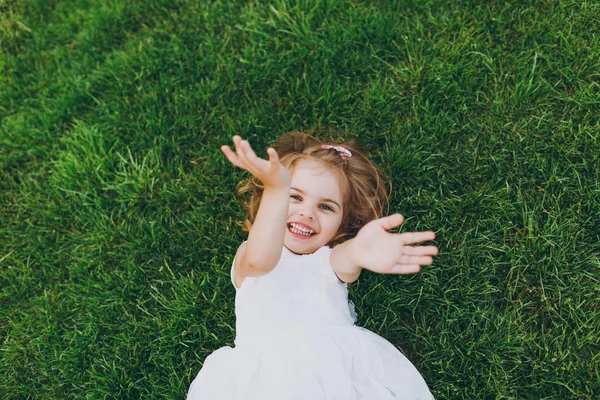 Parkta el sallayarak gülen güzel çocuk bebek, küçük kız ışık elbise yalan yeşil çim çim, üzerine. Anne, küçük çocuk kızı. Anneler günü, aşk aile, ebeveynlik, çocukluk kavramı