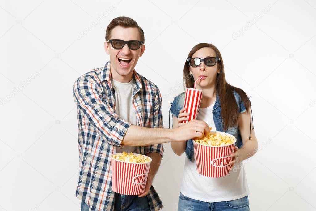 Young laughing couple, woman and man in 3d glasses watching movie film on date holding bucket of popcorn, plastic cup of soda or cola stealing popcorn isolated on white background. Emotions in cinema