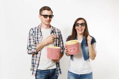 Genç çift, kadın ve erkek 3d gözlük ve rahat kıyafetler tarihte, film film izlerken patlamış mısır, gülüyor, poiting parmağı beyaz arka plan üzerinde izole kova tutarak. Sinema duygular