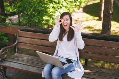 Hafif rahat kıyafetler genç kadın. Bitcoin sikke altın renk modern dizüstü pc bilgisayar açık havada sokakta üzerinde tutarak bankta oturan kadın. Mobil ofis sanal para kavramı