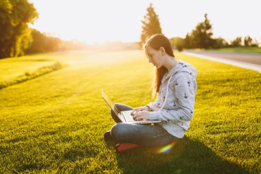 Genç öğrenci kadın rahat kıyafetler. Dizüstü pc bilgisayar Şehir Park açık havada Güneş çim yeşil çim üzerinde çalıştığı yer, çimenlerin üzerinde oturan bir bayan. Mobil ofis. Serbest iş kavramı