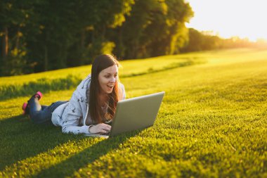 Genç öğrenci rahat kıyafetler içinde kadın akıllı. Çim, dizüstü pc bilgisayar Şehir Park açık havada Güneş çim yeşil çim üzerinde üzerinde çalışıyor yatan kadın. Mobil ofis. Serbest iş kavramı