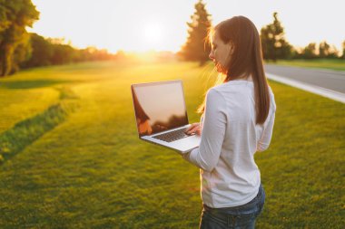 Genç kadın arkadan görünüm. Şehir Parkı yeşil çim Güneş'ın bahçesinde açık havada, uzay kopyalamak için dizüstü pc bilgisayar boş siyah Boþ ekran ile üzerinde çalışan kadın. Mobil ofis. Serbest iş kavramı