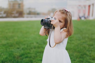 Işık elbiseli küçük güzel çocuk bebek kız parkta yeşil çimenlerin üzerinde retro vintage fotoğraf makinesinde resim çekmek. Anne, küçük çocuk kızı. Anneler günü, aşk aile, ebeveynlik, çocukluk kavramı